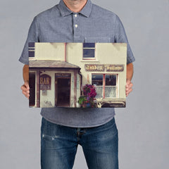 A man wearing a blue-gray polo shirt and jeans holds a rectangular 45x30CM canvas print showing a vintage-style pub exterior with the sign 'Teddy Sullivan' and flower boxes.