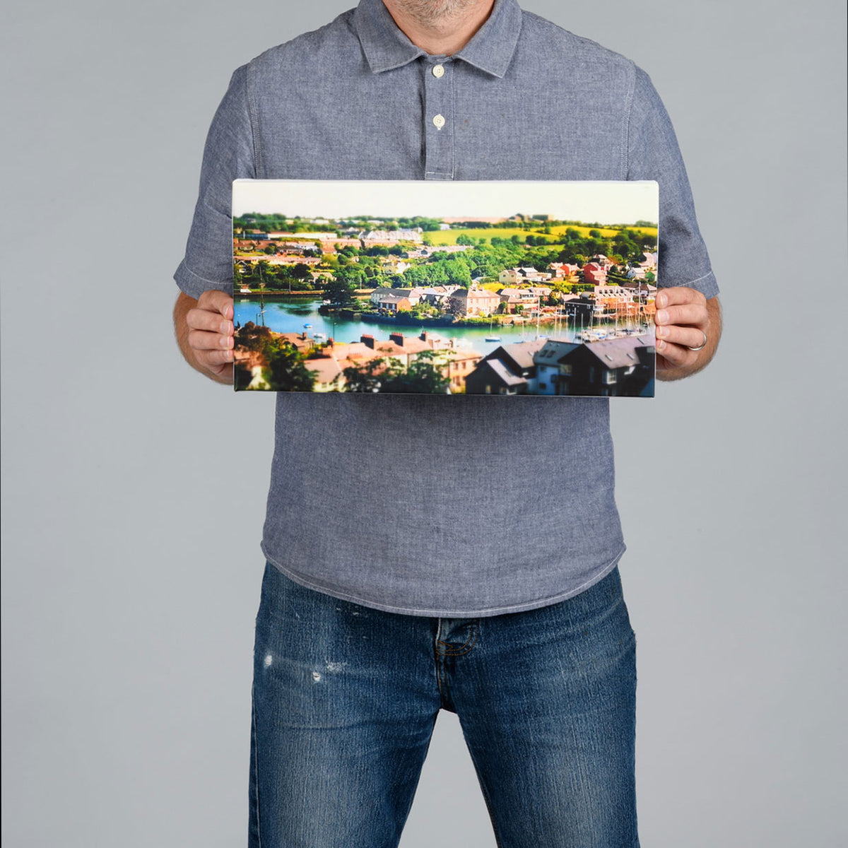 A man holding a panoramic shaped canvas print featuting Kinsale harbour. 