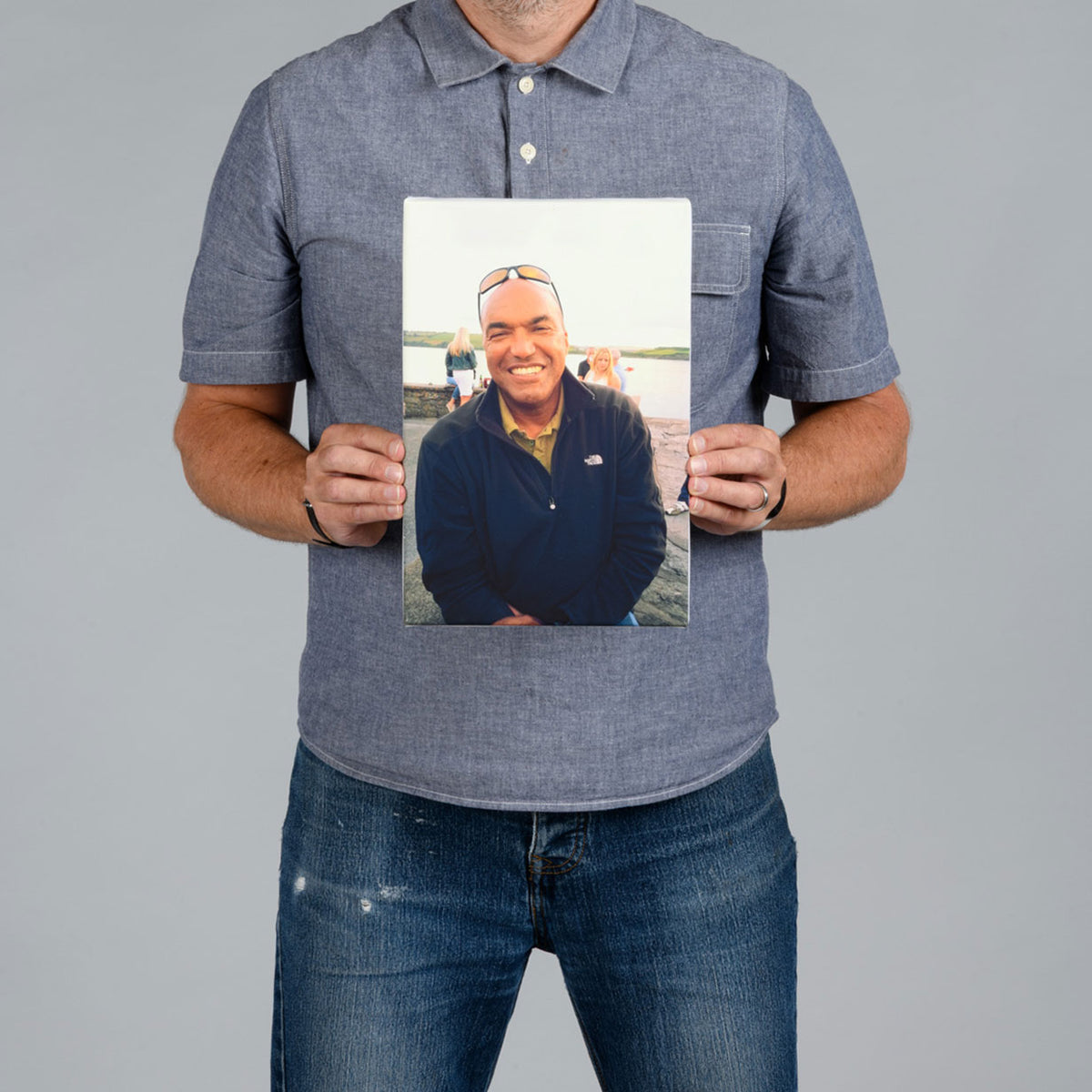 A man holding a portrait rectangle canvas print of a man sitting by the water